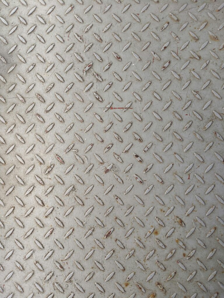 Close-up of a textured metal surface featuring a rustic diamond plate pattern, ideal for industrial backgrounds.