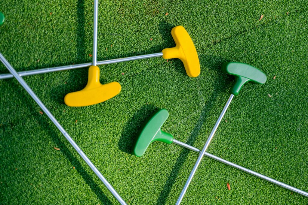 Vibrant yellow and green mini golf putters arranged on a lush green turf, perfect for leisure scenes.